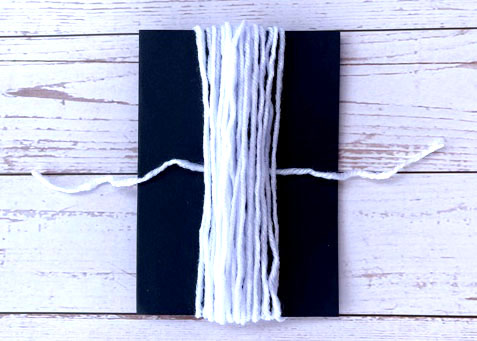 Grab the yarn and cut a 10" piece. Then slip it under the wrapped yarn on the cardstock.